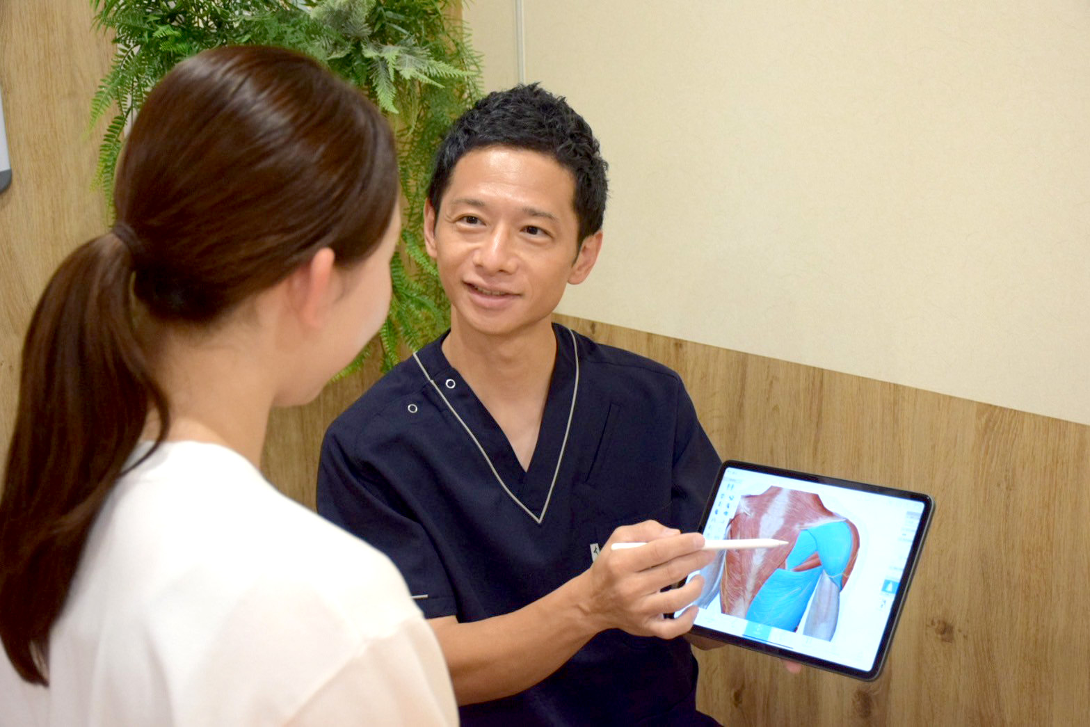 タブレットで筋肉の図を示して患者に説明をする柔道整復師